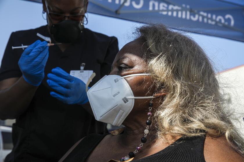Los Angeles, CA - July 16: Eon Walk, left, administers a Pfizer-BioNTech vaccine to Elwarder Silas at a mobile COVID-19 vaccine clinic, hosted by Mothers In Action in collaboration with L.A. County Department of Public Health at Mothers in Action on Friday, July 16, 2021 in Los Angeles, CA. (Irfan Khan / Los Angeles Times)
