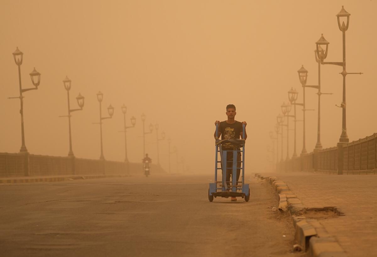 Un hombre empuja una carretilla durante una tormenta de arena el lunes 23 de mayo de 2022, en Bagdad, Irak.