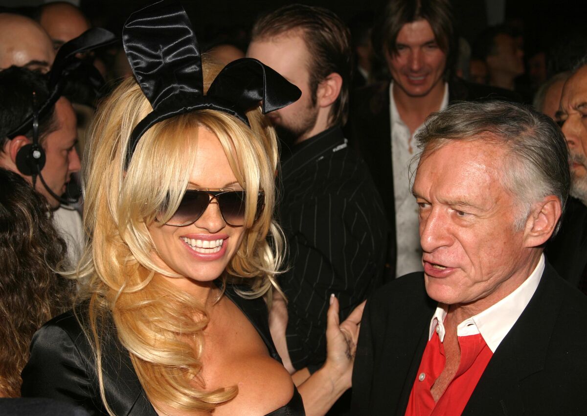 A blond woman in sunglasses and bunny ears stands with an older man at a party.