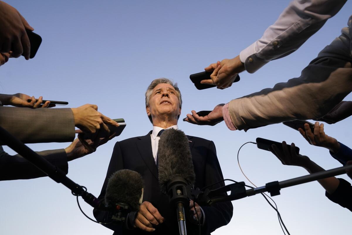 U.S. Secretary of State Antony J. Blinken speaks while recording devices are thrust toward his face 