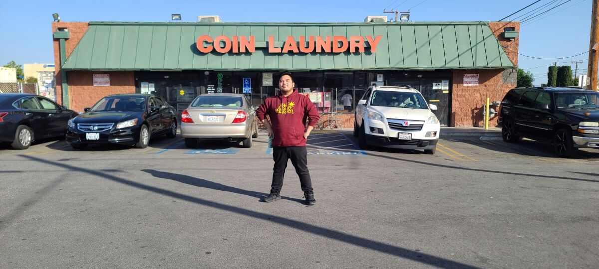 A man in a red hoodie stands in front of a laundromat.