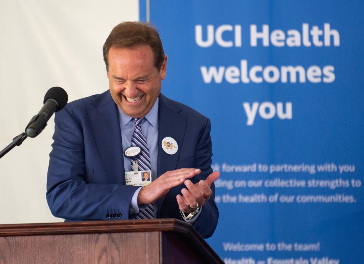 Fountain Valley Regional Hospital CEO Randy Rogers applauds in front of a UCI Health banner.