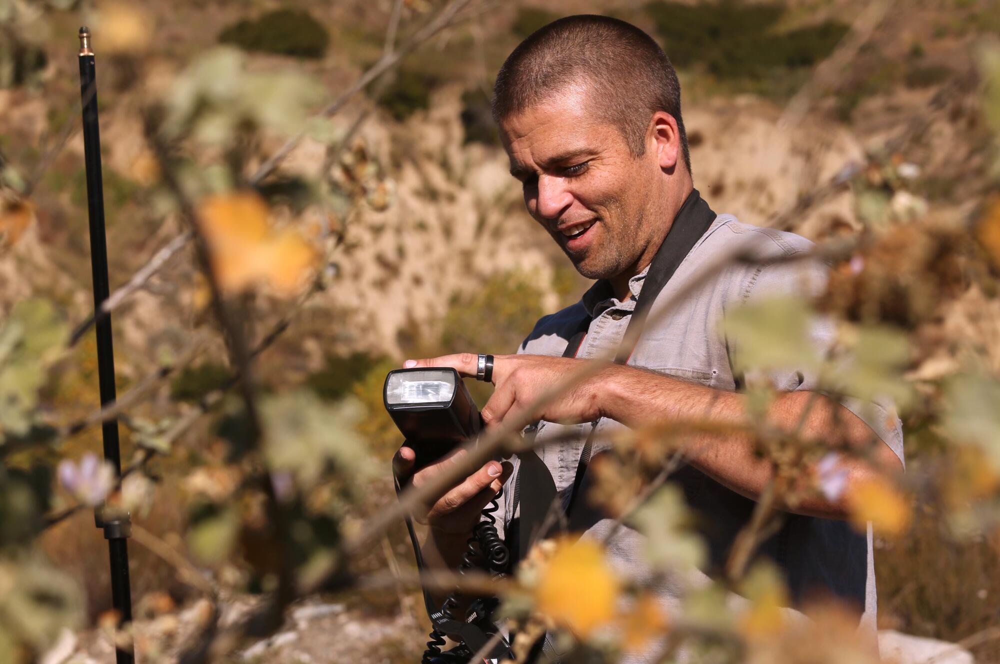 Surrounded by plants, a man looks down at his camera