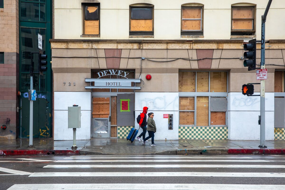 Two people walk past the boarded-up facade of the Dewey Hotel 