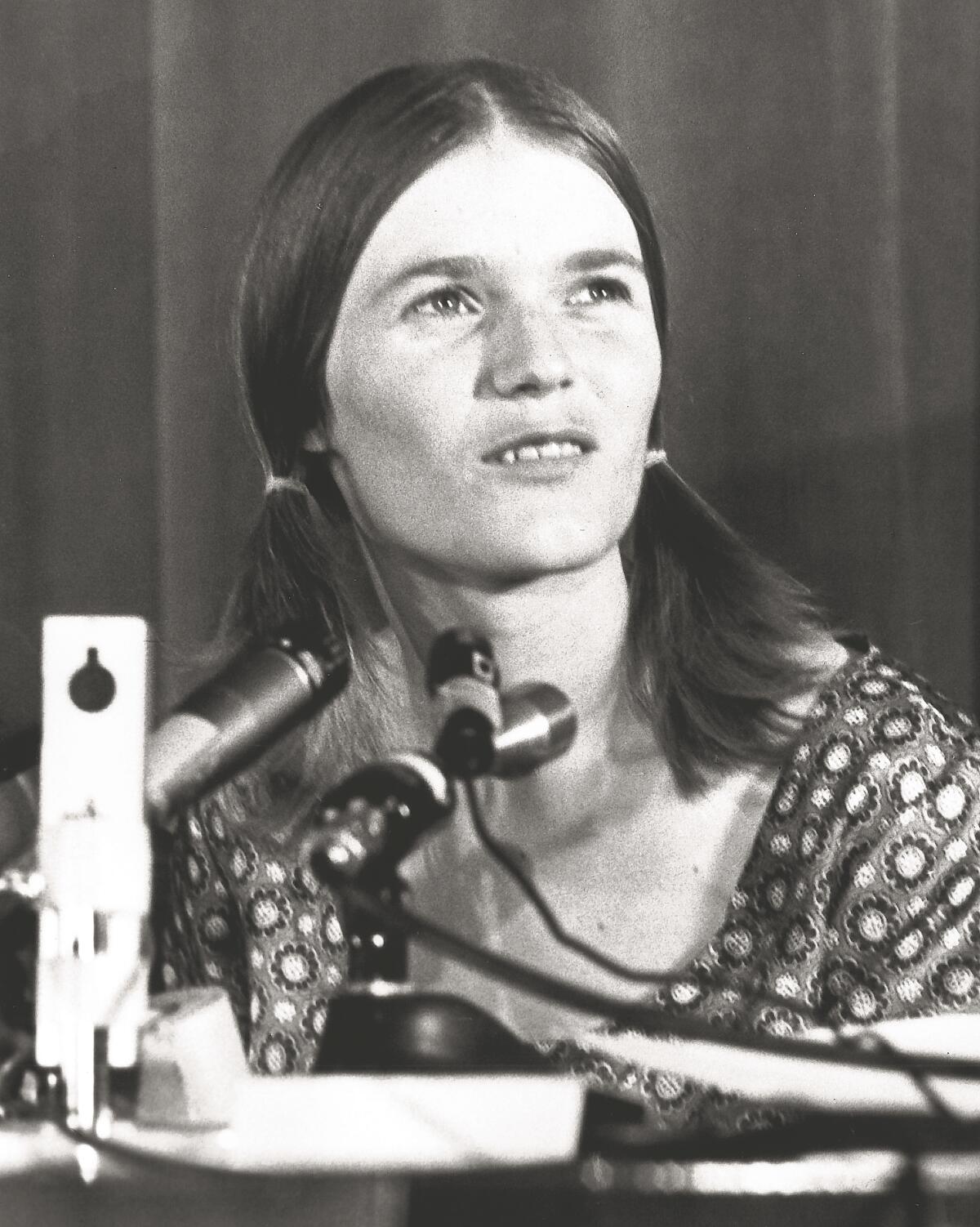 Closeup of a woman in pigtails talking into a bank of microphones.