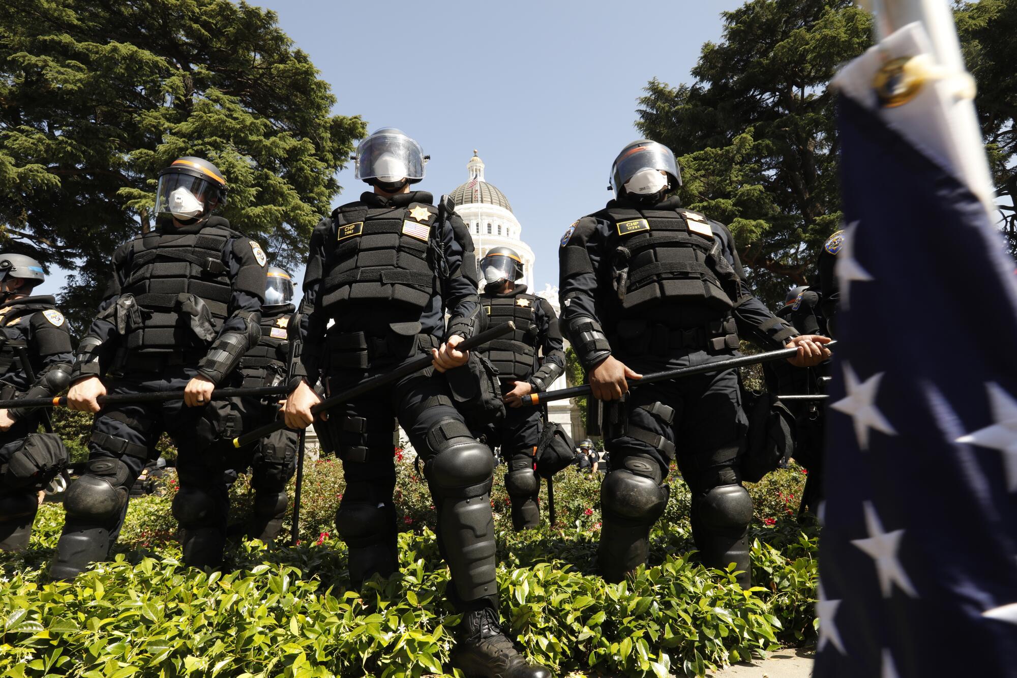 CHP officers wearing riot gear line the edge of the California State Capital grounds after removing protesters.