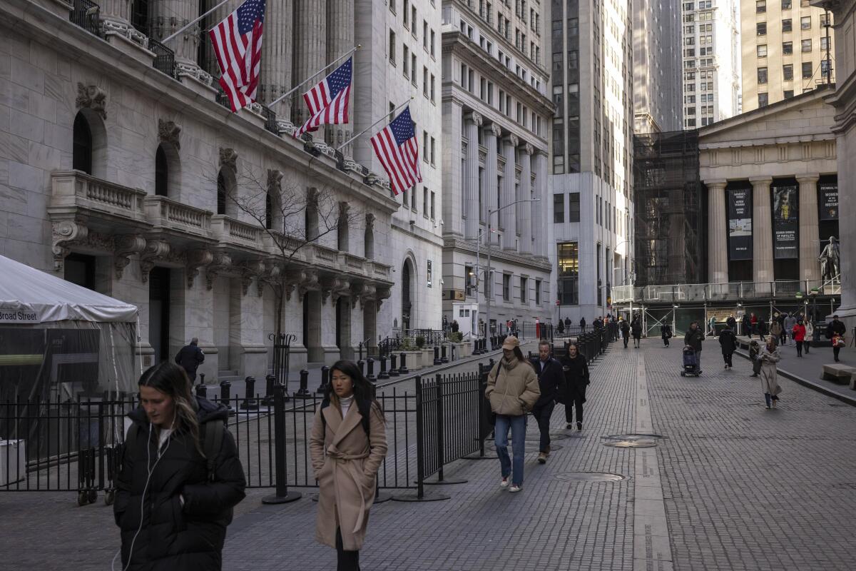 People walk past the New York Stock Exchange, which has flags hanging from its front. 
