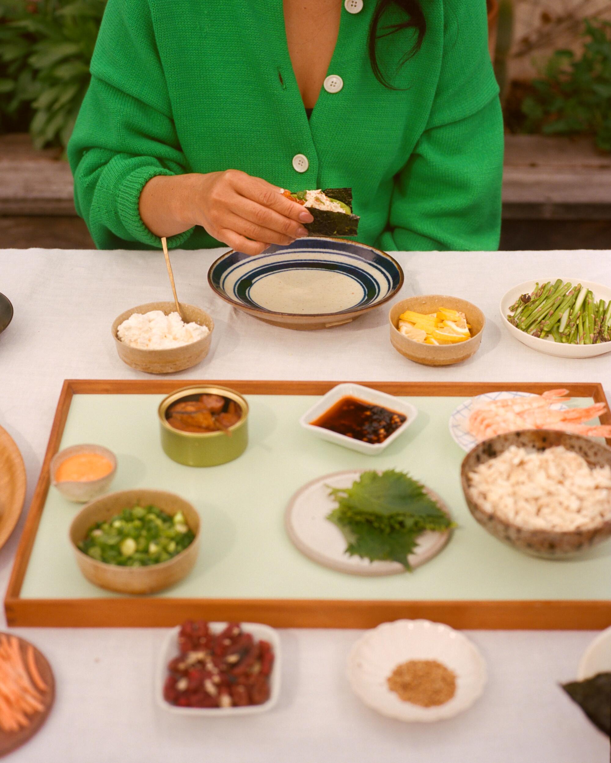 A person sits at a table with a selection of hand roll ingredients.
