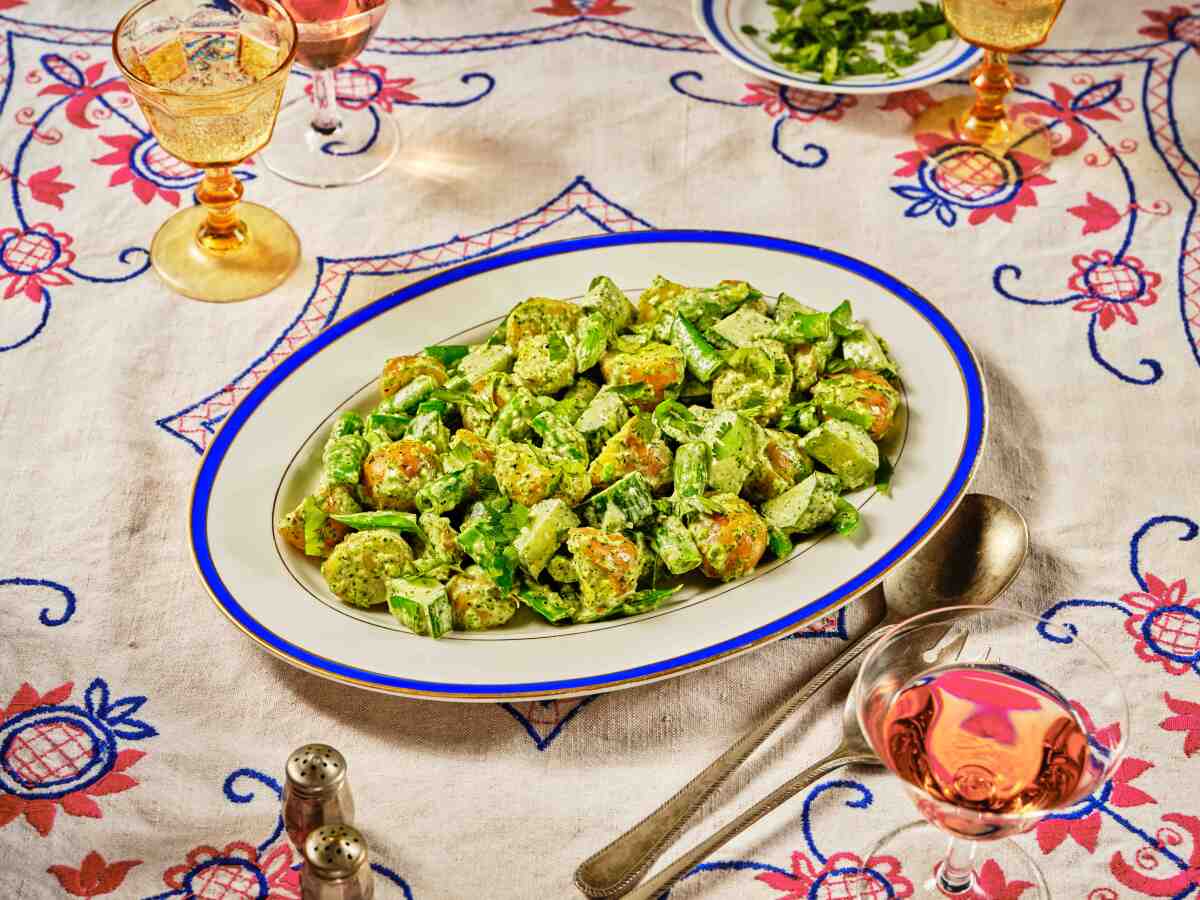 Green Potato Salad with Zhoug on a white plate with blue rim, sitting on a colorful tablecloth