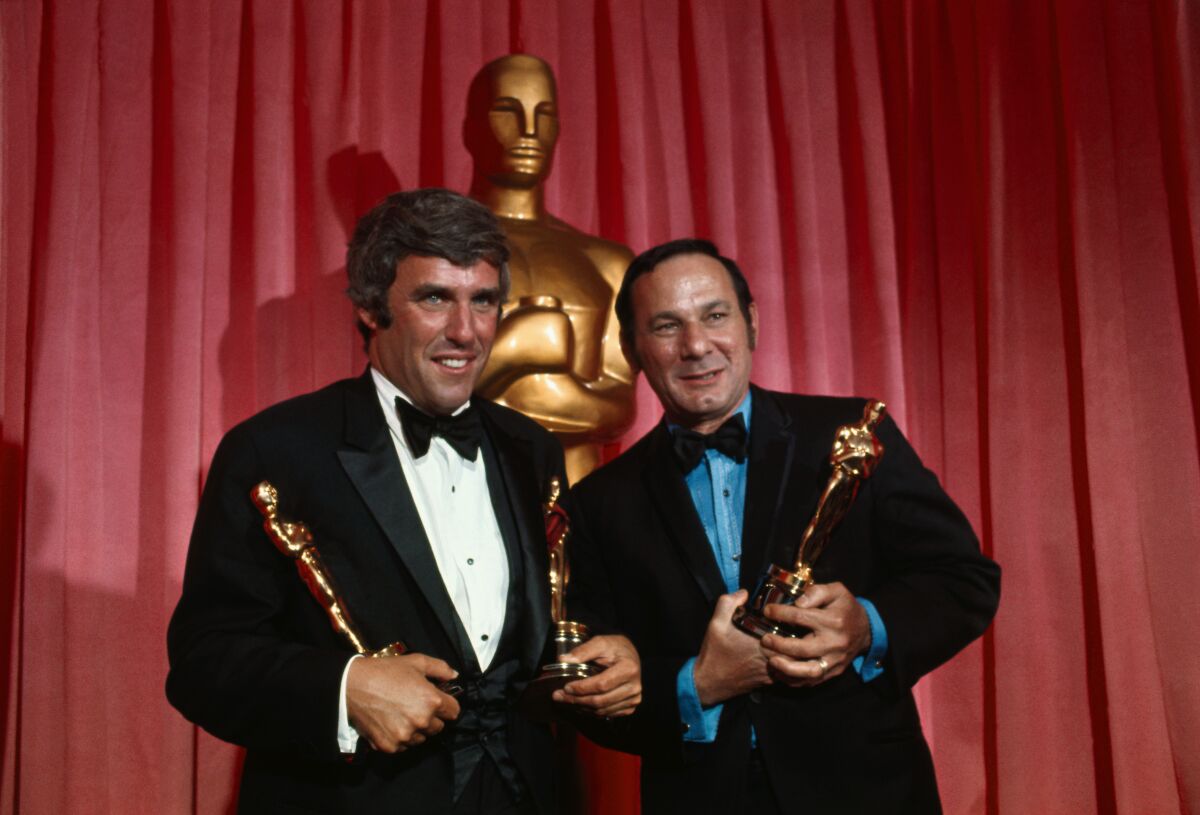 Two men in tuxedos hold Oscars