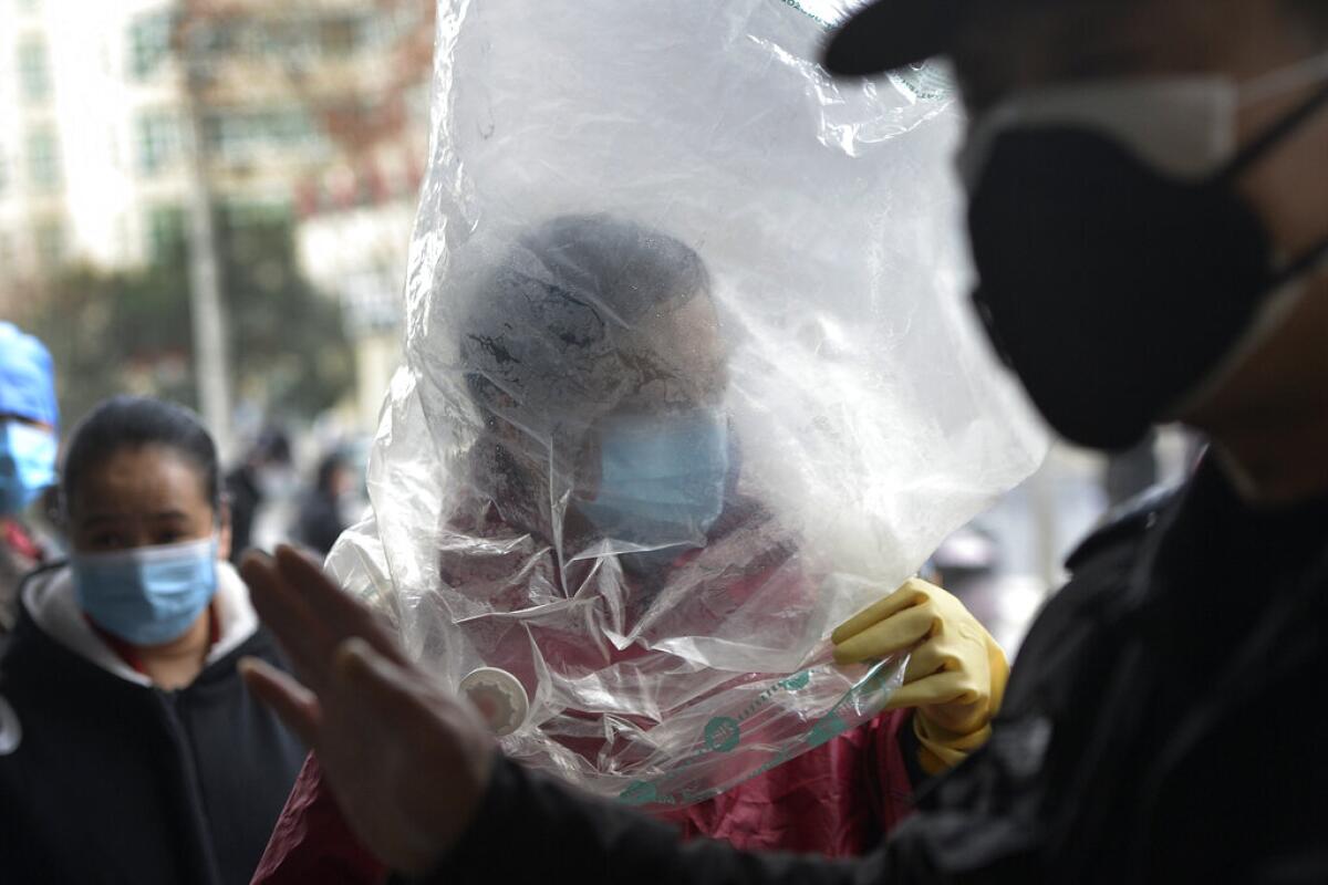 Un hombre con una mascarilla se cubre con un plástico antes de entrar en un supermercado en Wuhan, en la provincia central china de Hubei, el lunes 10 de febrero de 2020. (Chinatopix via AP)