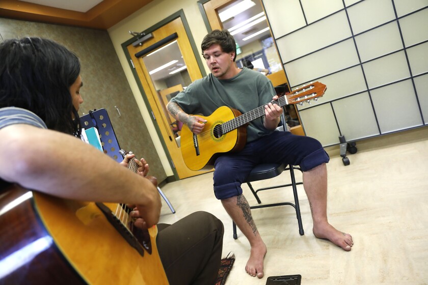  Doors of Change volunteer guitar teacher Taigro Pimentel, left, shows Sage Arnold, a homeless youth, a guitar chord.