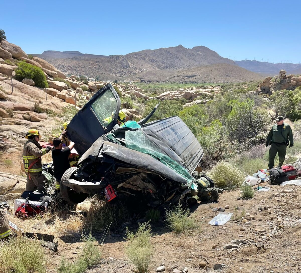 Authorities inspect the wreckage of a vehicle near boulders in a desert area 