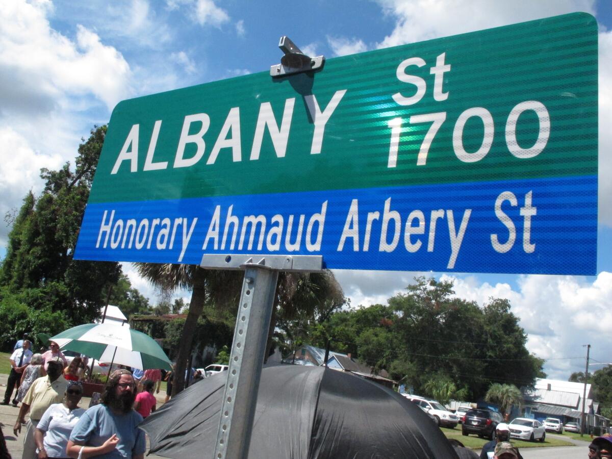 A crowd gathers under a new sign designating a city roadway as Honorary Ahmaud Arbery Street on Tuesday, Aug. 9, 2022, in Brunswick, Ga. City officials approved the honor for Arbery, a 25-year-old Black man who was fatally shot in February 2020 after being chased by three white men in pickup trucks who spotted him running in their neighborhood. All three men were later convicted of murder and federal hate crimes. (AP Photo/Russ Bynum)