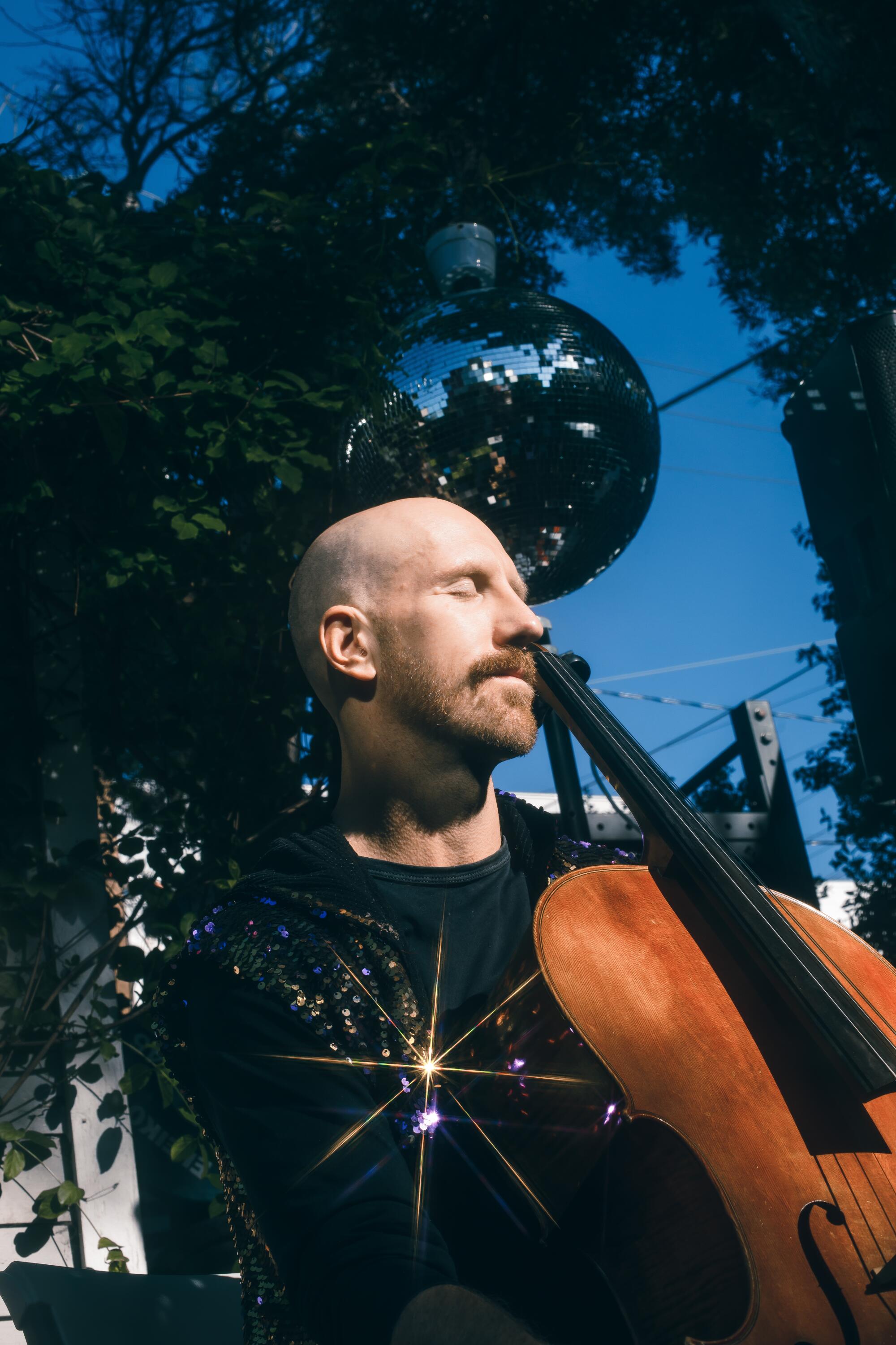 Evan Cudworth sits holding a cello in a backyard.