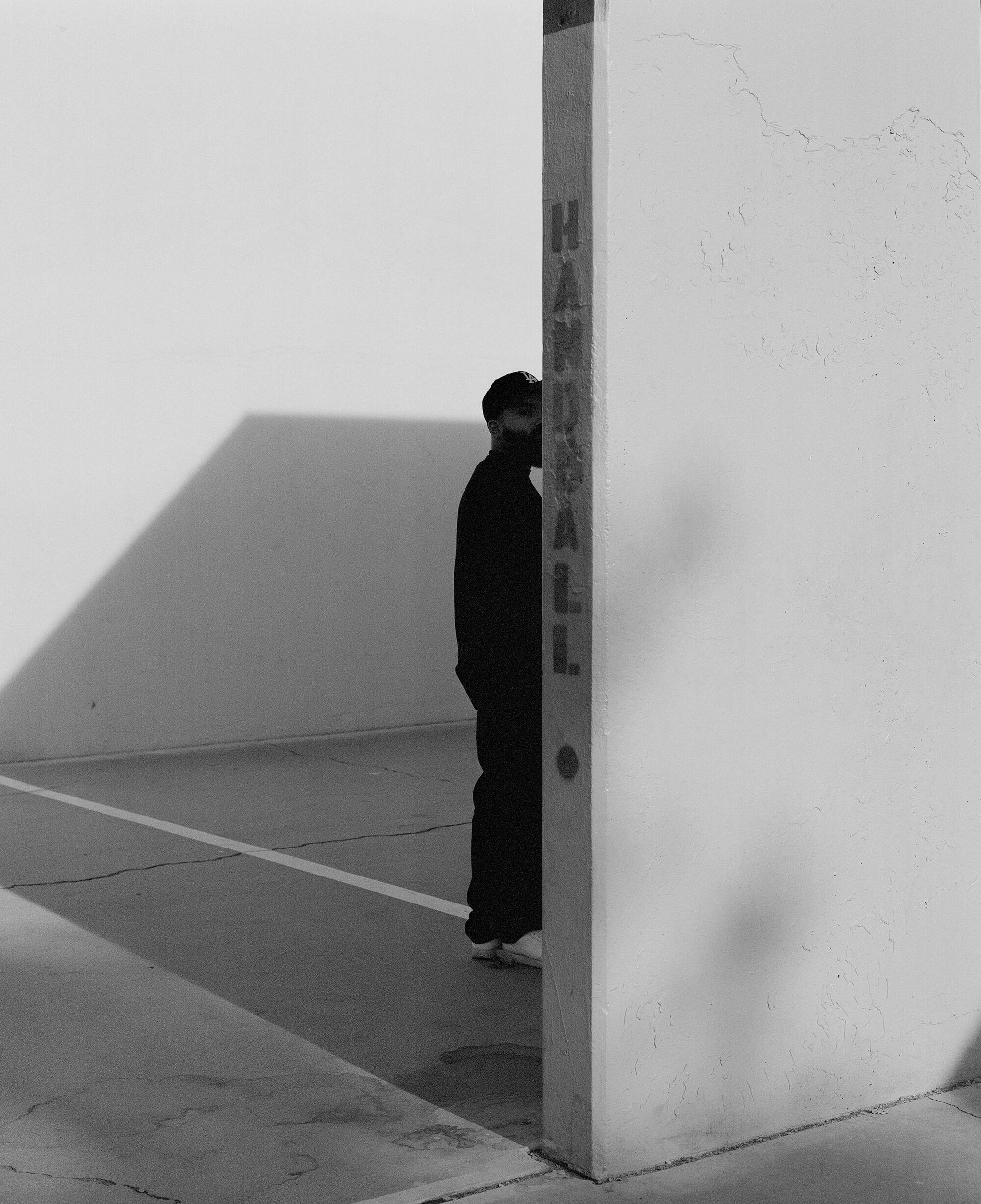 A black and white photo of the founder of ?edouze, Guillermo Juarez, standing behind a handball wall peeking at the camera