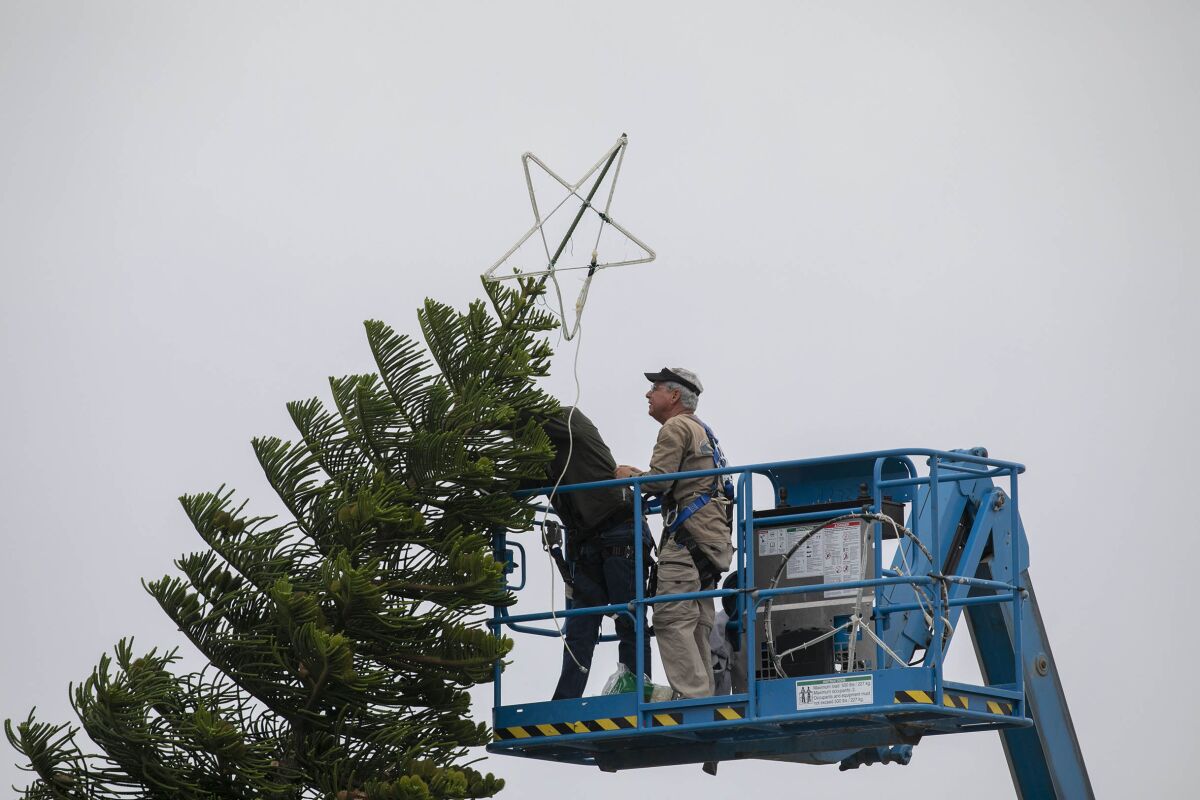 Ken Moss, right, and another volunteer with the Ocean Beach Town Council installed the star atop this years Ocean Beach Christmas tree at the foot of Newport Avenue on Tuesday, Dec. 3, 2019.
