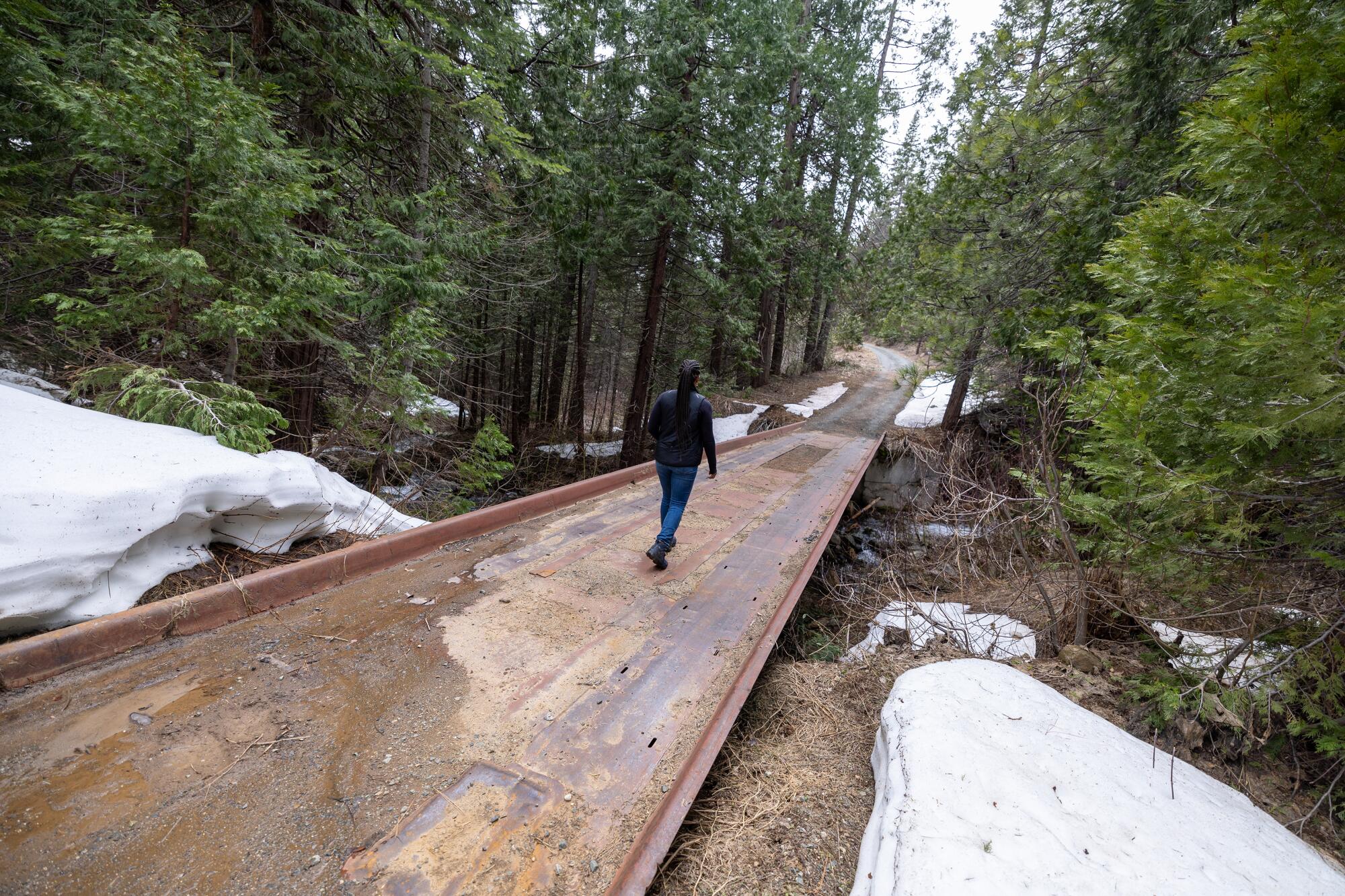 A woman walks over a bridge on a forested path.