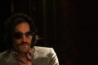 Vincent Gallo wears sunglasses and a gray blazer in a dark room.