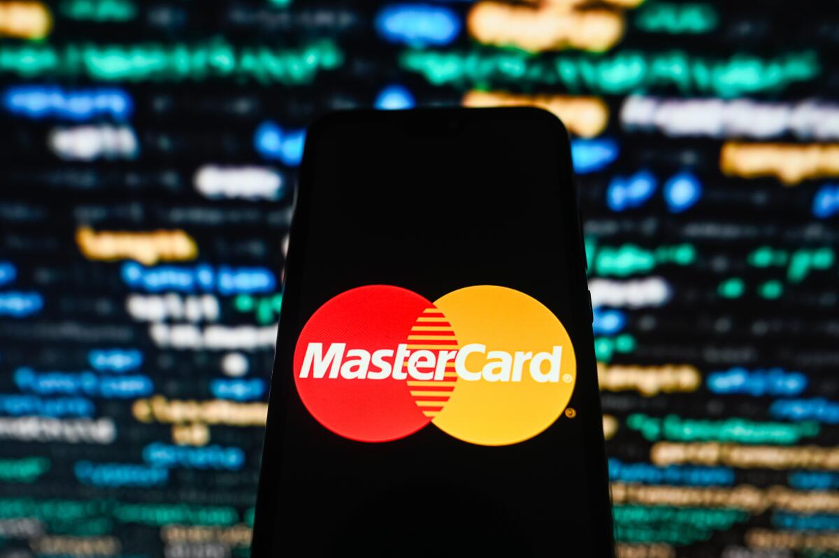 A Mastercard logo displayed on a smartphone with coding in the background.