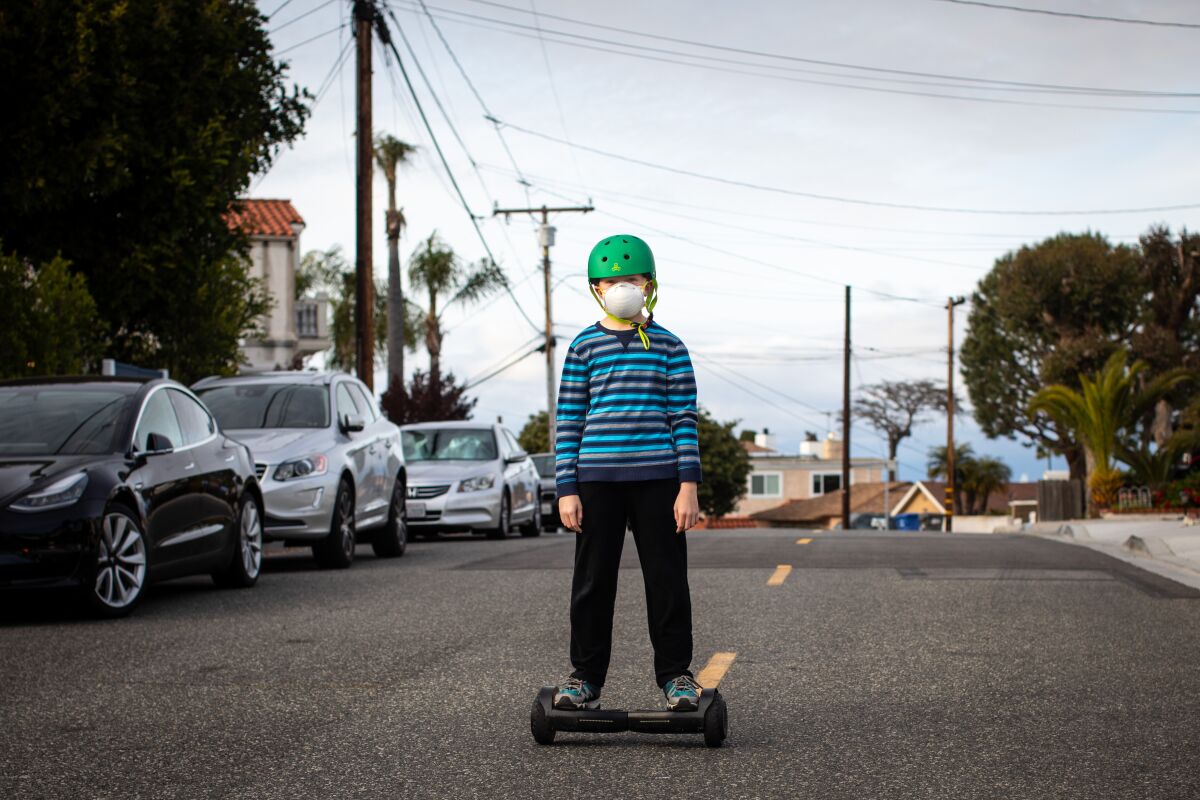 A masked child on a hoverboard in the middle of a street with no traffic