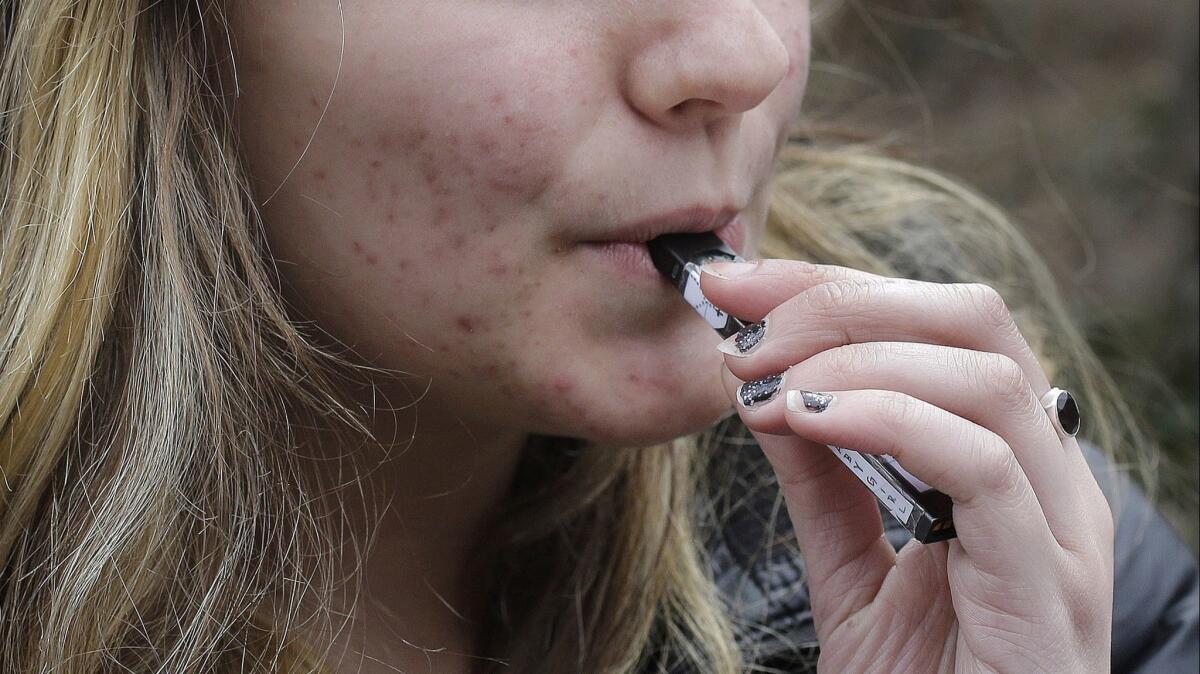 A teenager uses a vaping device near her school in Cambridge, Mass. A California bill to stop teen use of electronic cigarettes was shelved Thursday.