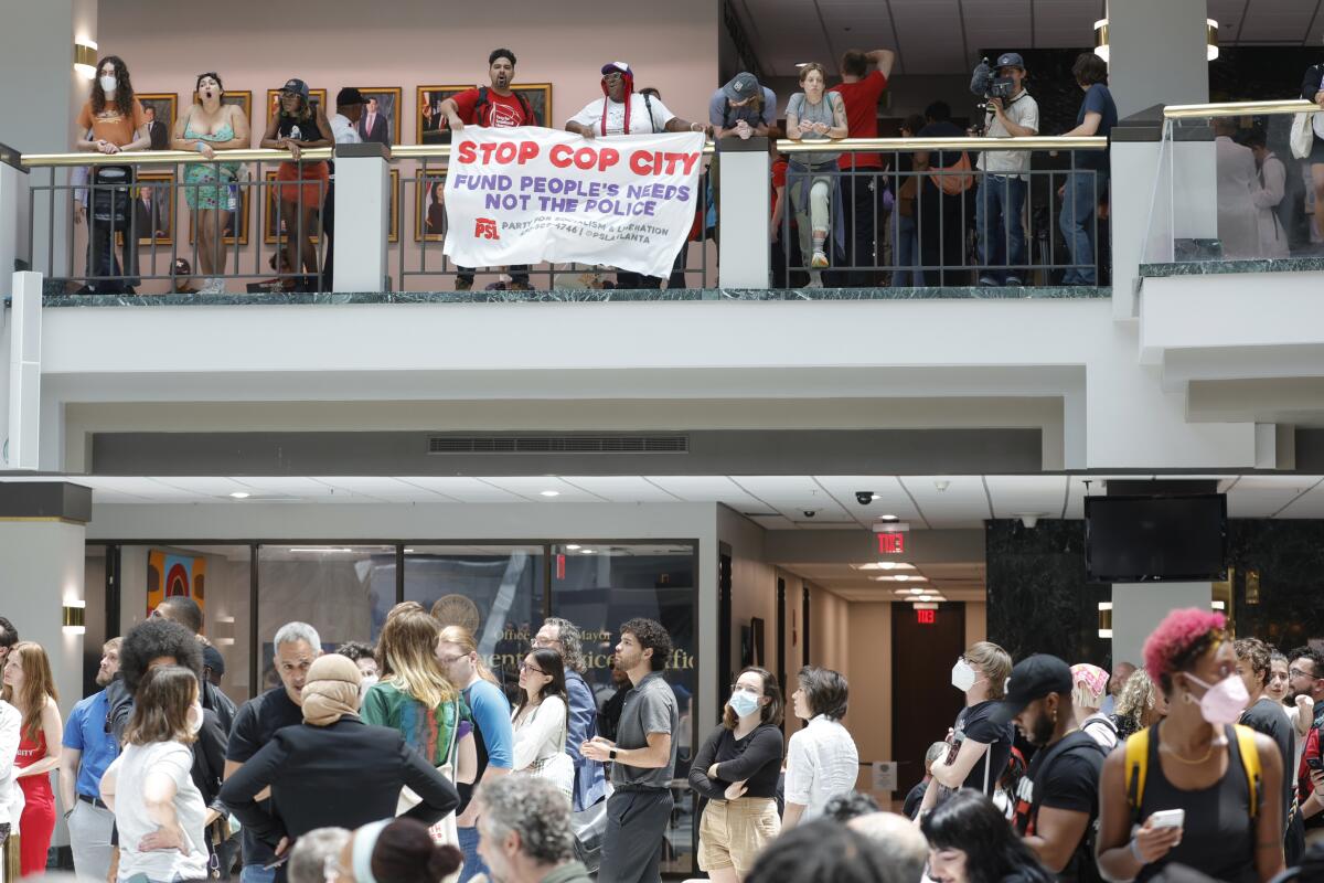 Protesters in Atlanta City Hall, with two holding a sign reading "Stop Cop City."