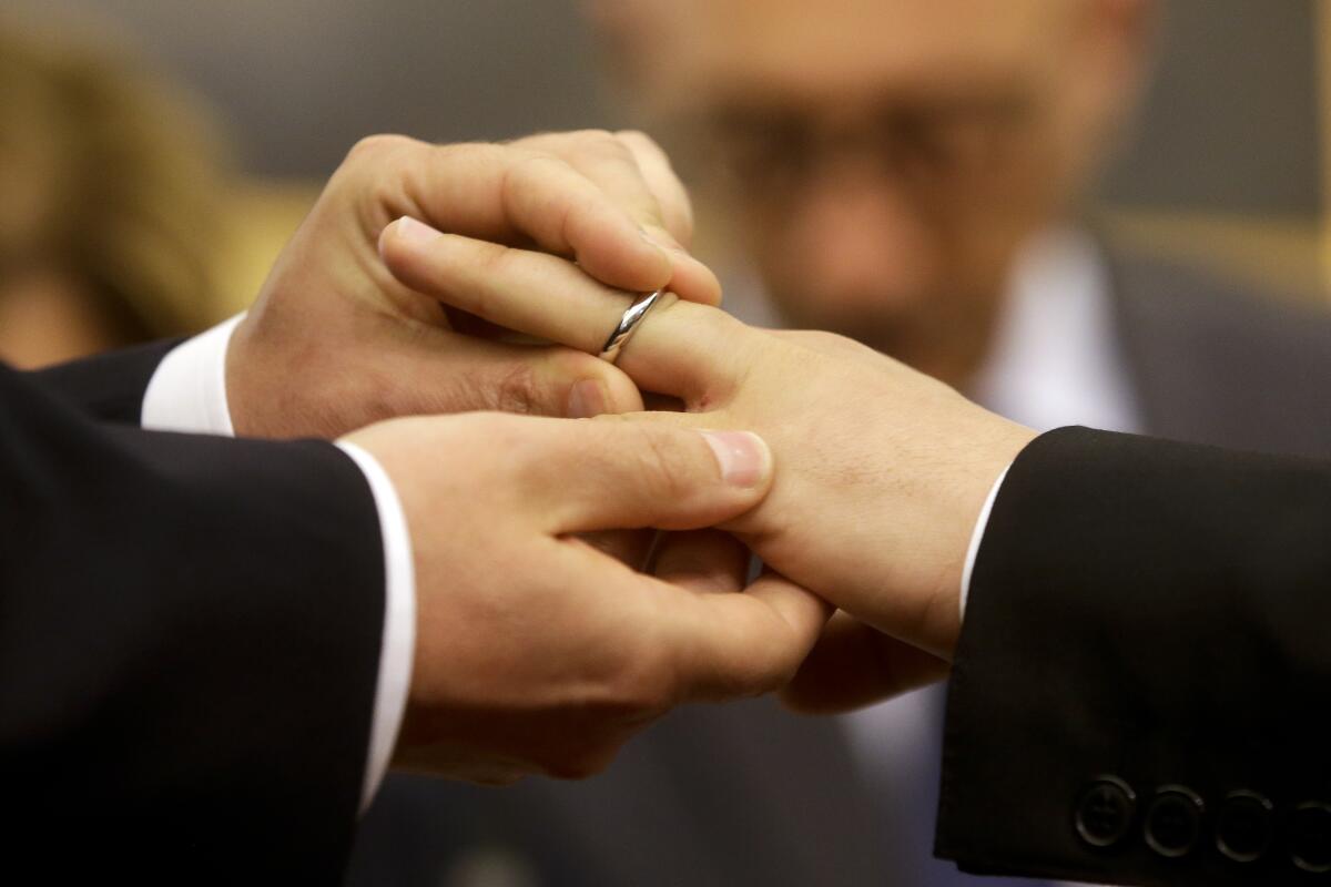 A man slips a wedding ring onto his partner's finger 