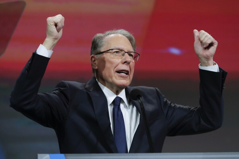 Wayne LaPierre lifts his arms into the air as he speaks into a microphone.