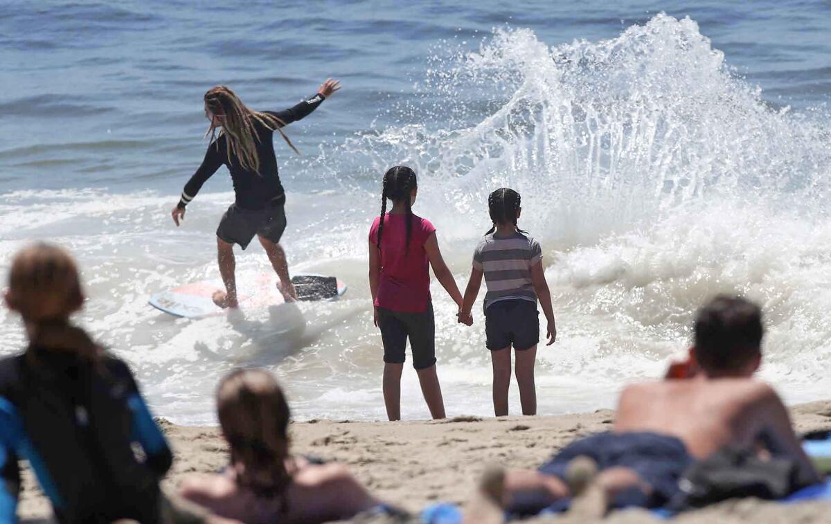 Beachgoers watch a skim boarder ride a wave at Aliso Beach Park in Laguna Beach on Friday.