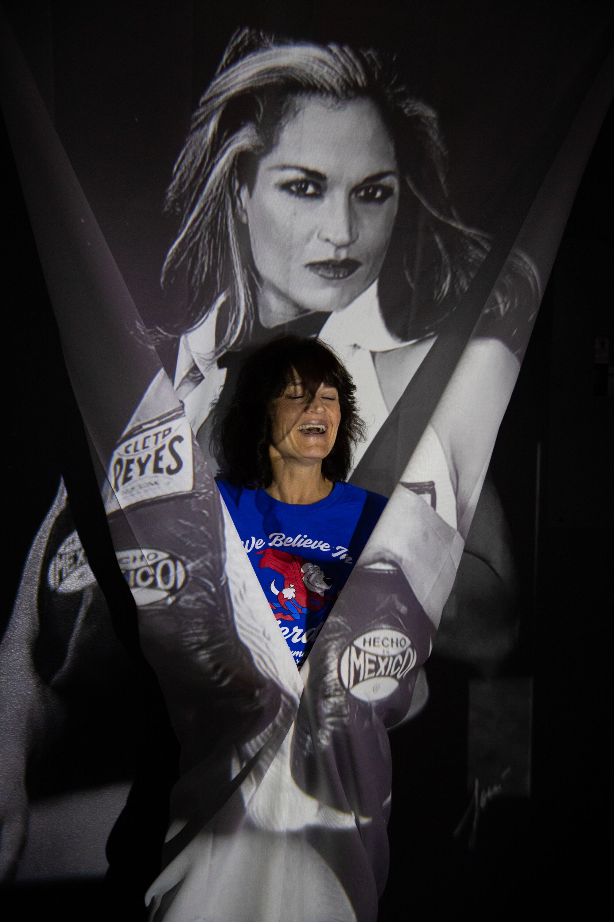 A woman stands in front of a larger image of a woman with boxing gloves in black and white.