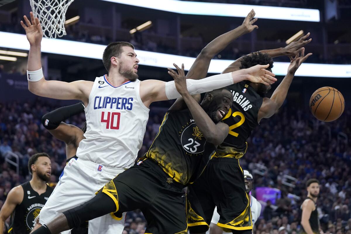 Clippers center Ivica Zubac reaches for the ball next to Warriors Draymond Green (23) and Andrew Wiggins.