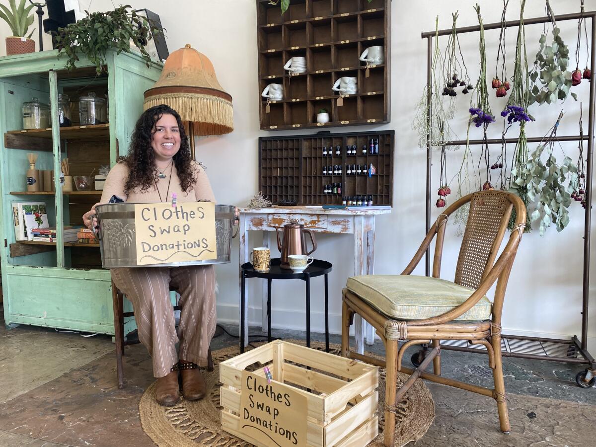 A woman sitting on a chair holding a bin with a sign that says "clothes swap donations."