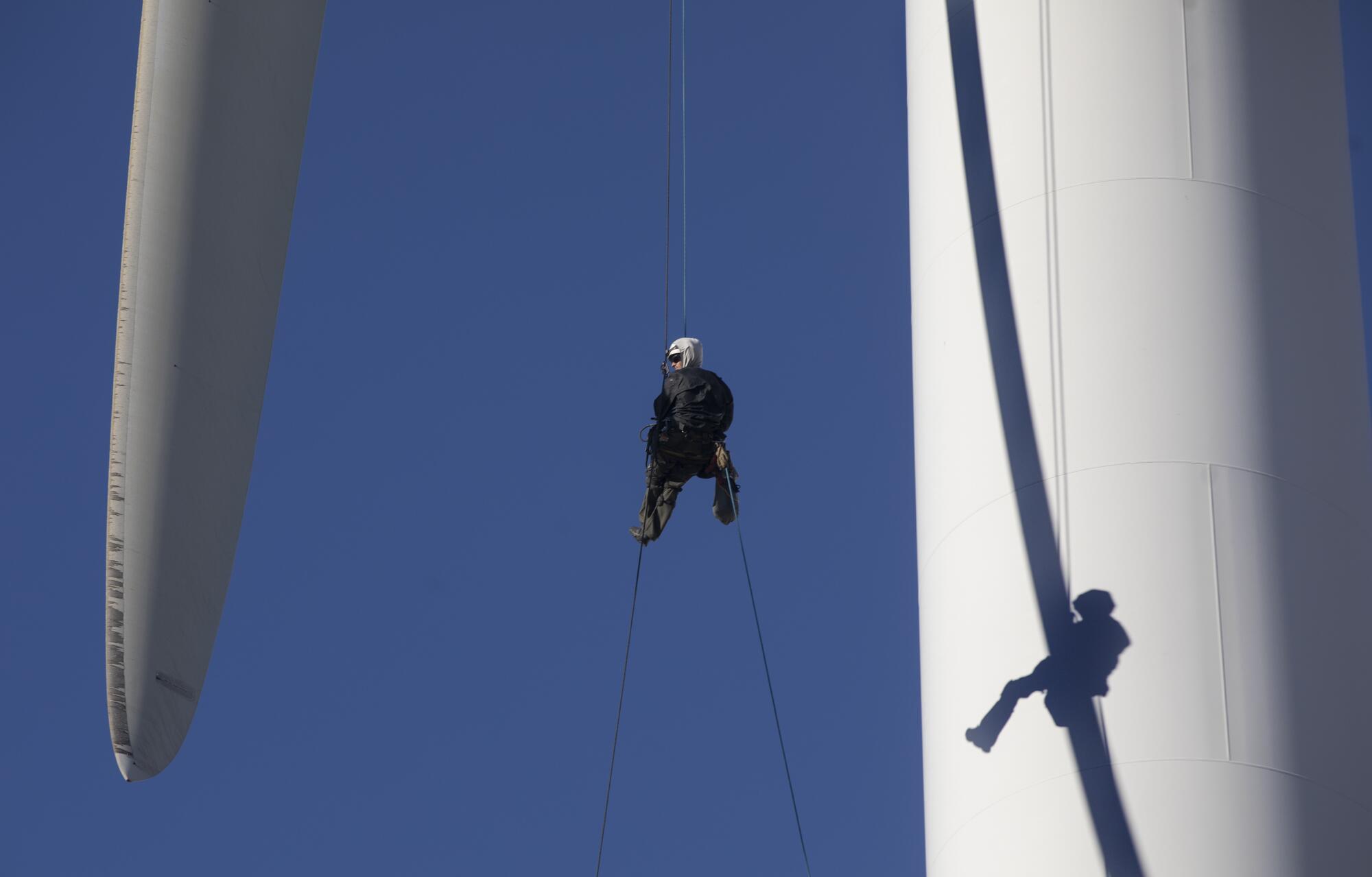 A person hangs from a wind turbine.