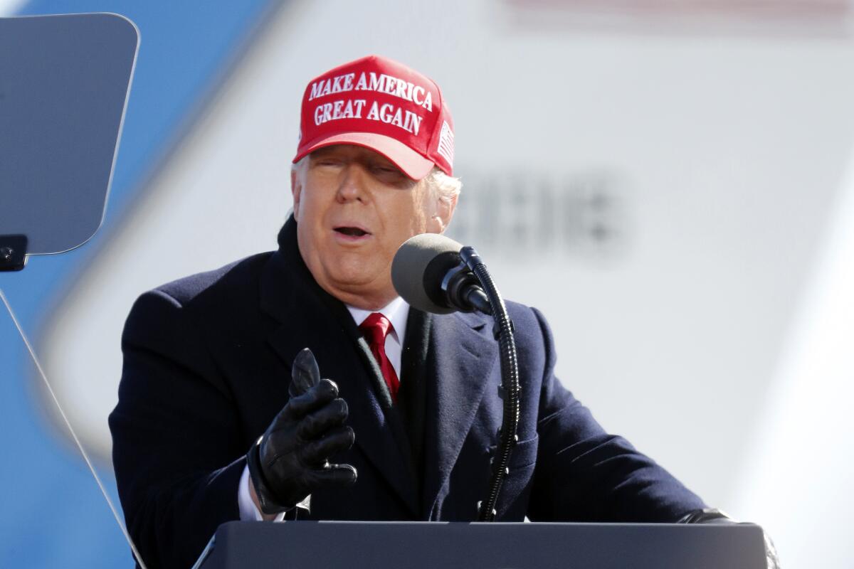 President Trump, in overcoat and MAGA hat, speaks at a rally.