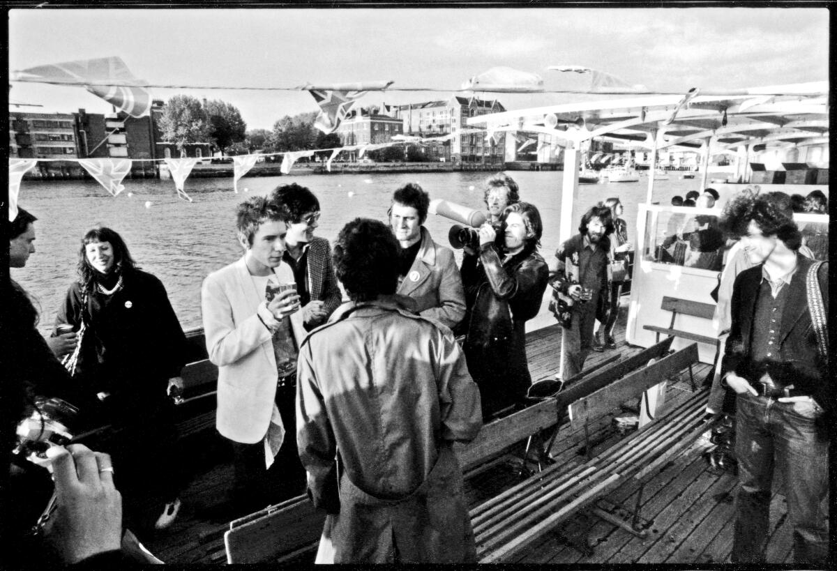 The Sex Pistols and artist Jamie Reid stand on a boat. 