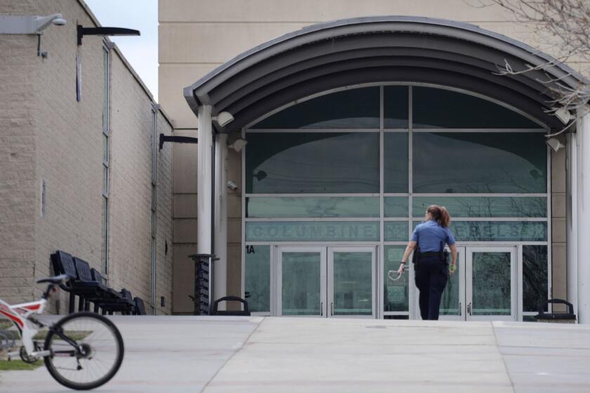 A police officer walks to the front doors of Columbine High School, Wednesday, April 17, 2019, in Littleton, Colo., where two student killed 12 classmates and a teacher in 1999. The school was closed along with hundreds of others in Colorado after an armed young Florida woman who was allegedly "infatuated" with Columbine threatened violence just days ahead of the 20th anniversary of the attack. (AP Photo/Joe Mahoney)