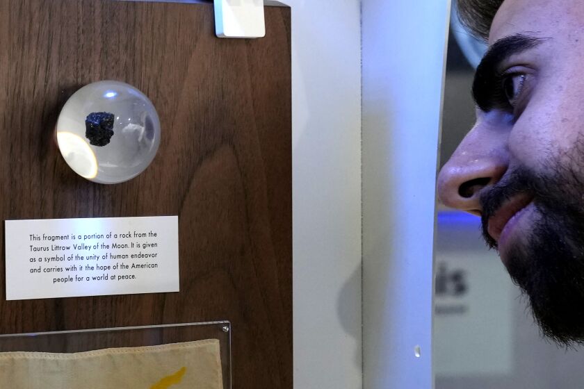 A spectator looks at a tiny piece of moon rock encased in a plastic globe, on display at the an exhibition commemorating the 50th anniversary of the last of the U.S. manned missions to the moon and the Artemis spacecraft now orbiting the moon, in Nicosia, Cyprus, Thursday, Dec. 8, 2022. A half century after U.S. astronauts brought it back from the moon's surface, this tiny piece of cosmic rock has finally reached its intended destination, the east Mediterranean island nation of Cyprus. (AP Photo/Petros Karadjias)