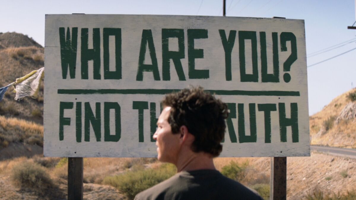 A man standing in front of a sign that reads, "Who Are You? Find The Truth?"
