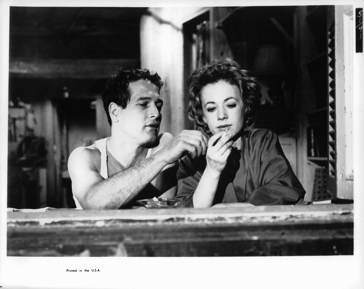 A black-and-white movie still shows a man and a woman sitting at a bar sharing a cigarette.