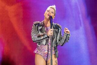 Pink in her signature updo with a studded and bejeweled leather jacket and pink body suit holding a microphone