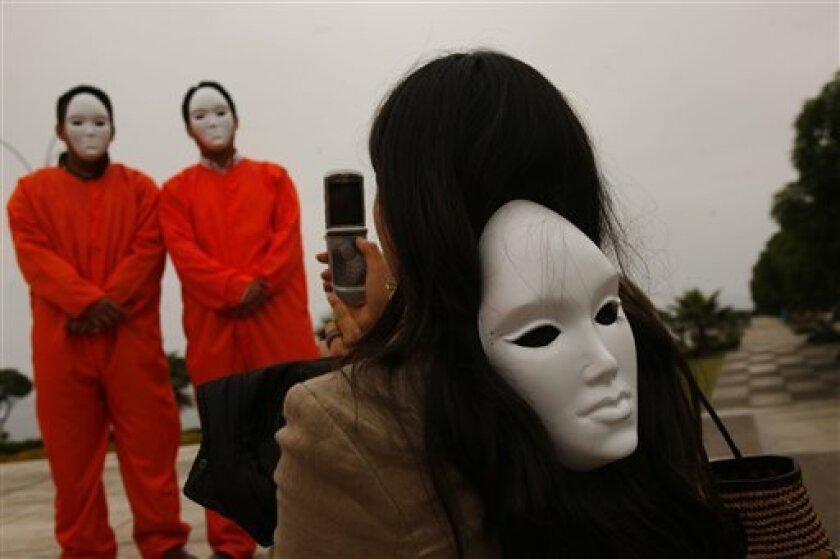 A demonstrator with a mask hanging on her back takes pictures of activists during a protest to demand the closing of the military prison at the US military base in Guantanamo in Lima, Wednesday, Nov. 19, 2008. President George W. Bush will arrive in Lima on Friday to attend the Asia Pacific Economic Cooperation leaders summit. (AP Photo/Dado Galdieri)