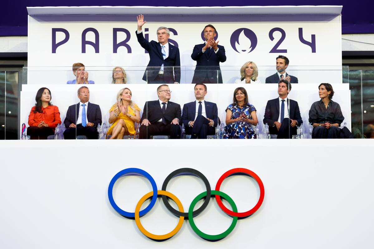 IOC President Thomas Bach waves while standing next to French president Emmanuel Macron 