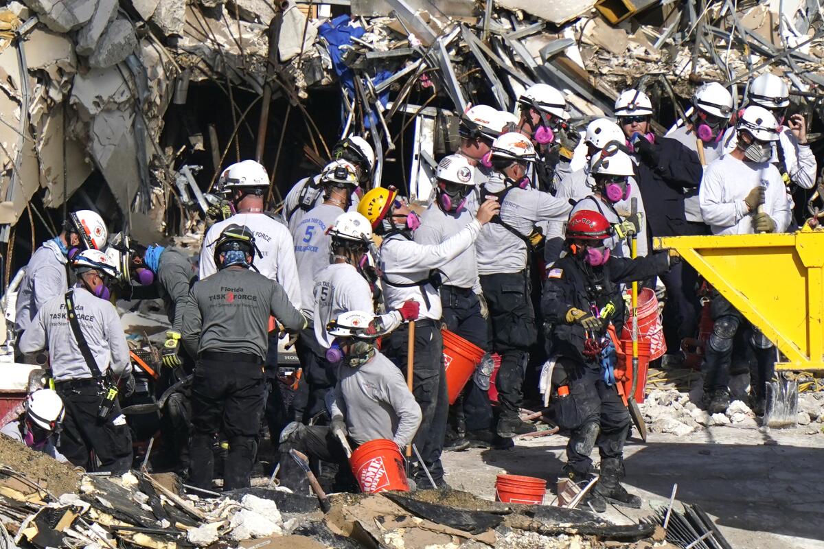 People in hard hats and face masks stand on rubble.