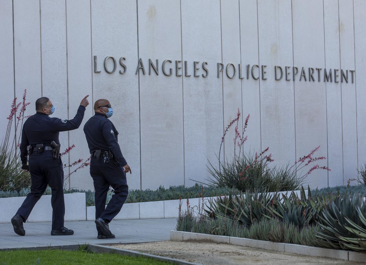 Two men in uniform and masks walk past a building with the sign "Los Angeles Police Department."
