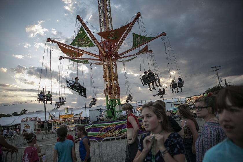 People wait to ride a revolving swing at the Perry State Fair in New Lexington, Ohio, Friday, July 24, 2020. In the towns that speckle the Appalachian foothills of southeast Ohio, the pandemic has barely been felt. Coronavirus deaths and racial protests _ events that have defined 2020 nationwide _ are mostly just images on TV from a distant America. (AP Photo/Wong Maye-E)