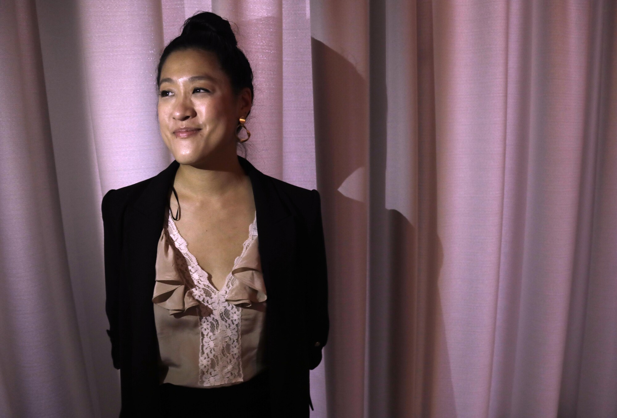 A woman stands in front of a pink curtain.
