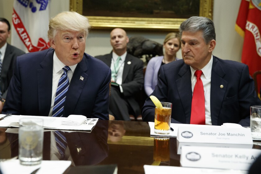 Joe Manchin and Donald Trump are seated at a table at the White House. 