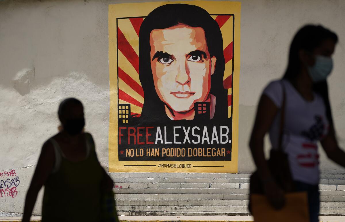 People walk near a poster depicting a man with dark hair and the words "Free Alex Saab"