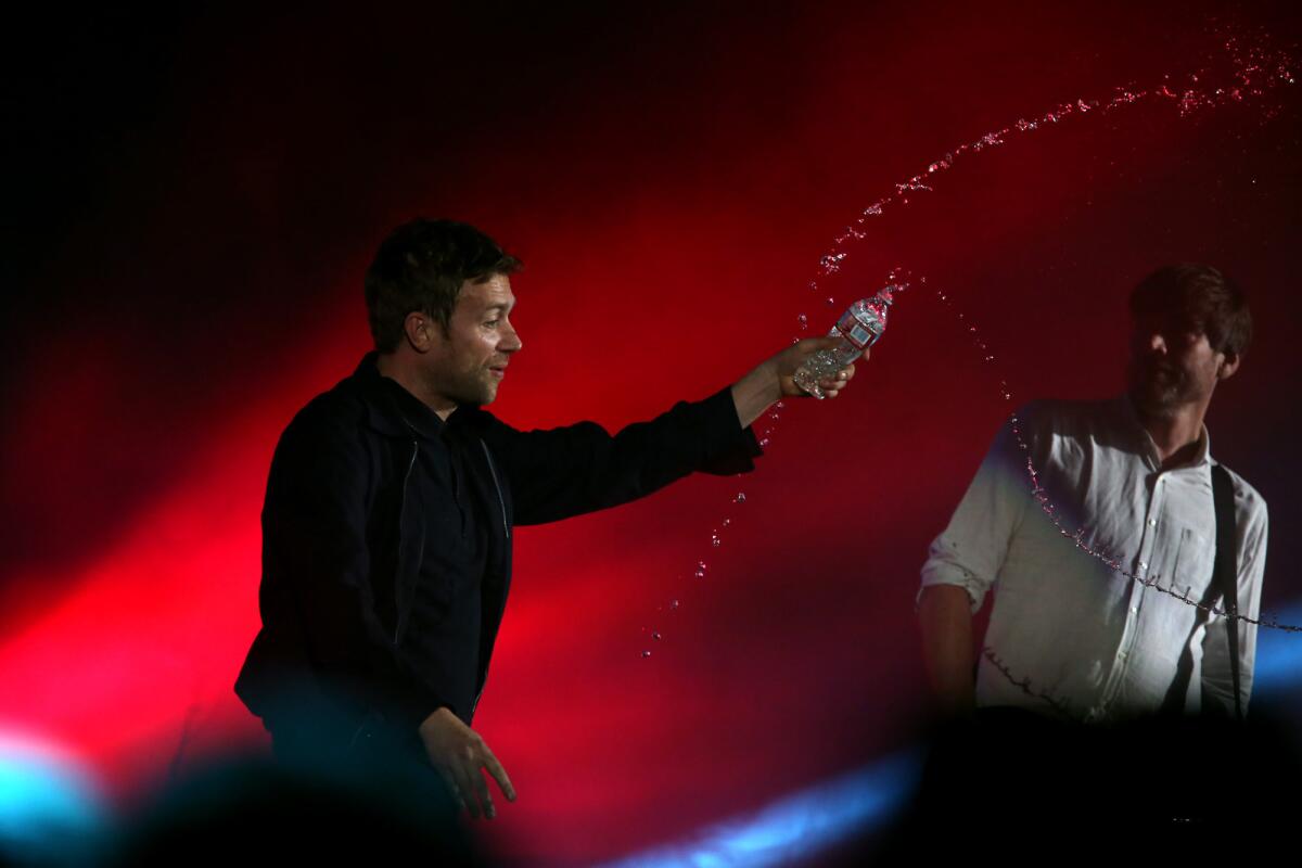 Singer Damon Albarn, left, throws water at the crowd as bassist Alex James looks on while they perform with Blur at the Hollywood Bowl.